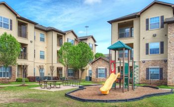 a playground with a slide and picnic table in front of an apartment building